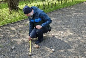 Powiększ zdjęcie: mężczyzna odmierzający odległość pomiędzy rzuconymi boulami
