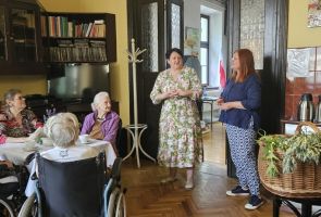 Powiększ zdjęcie: dwie kobiety podczas powitania uczestników spotkania w kawiarni dps