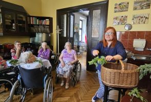 Powiększ zdjęcie: zielaska podczas prelekcji, obok słuchające kobiety przy stoliku