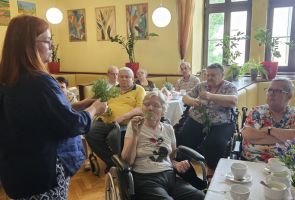Powiększ zdjęcie: zielarka podczas prelekcji, widok na kawiarnię wypełnioną Mieszkańcami dps