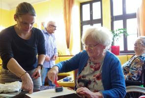 Powiększ zdjęcie: dwie kobiety przy stoliku, jedna robi odbitkę linorytu a druga jej pomaga