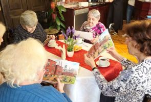 Powiększ zdjęcie: kobiety siedzące przy stoliku i oglądające miniaturę obrazu