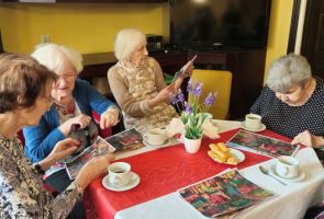 Powiększ zdjęcie: kobiety siedzące przy stoliku i oglądające miniaturę obrazu