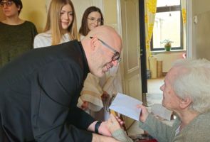 Powiększ zdjęcie: ksiądz w towarzystwie aniołów składający życzenia starszej kobiecie