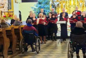 Powiększ zdjęcie: kobieta recytująca poezję, za nią członkowie chóru