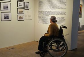 Powiększ zdjęcie: kobieta na wózku oglądająca fragment wystawy