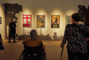 Powiększ zdjęcie: nasi Mieszkańcy słuchający oprowadzającej po wystawie kobiety