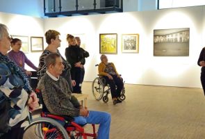 Powiększ zdjęcie: nasi Mieszkańcy słuchający oprowadzającej po wystawie kobiety