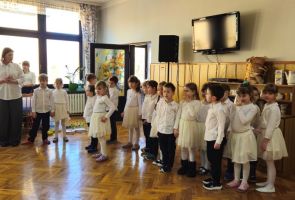 Powiększ zdjęcie: dzieci ubrane na biało z nauczycielką stoją w rzędzie na powitanie