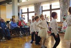 Powiększ zdjęcie: tańczące dzieci, w tle Mieszkańcy oglądający występ