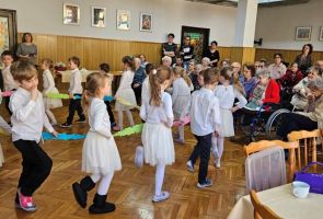 Powiększ zdjęcie: tańczące dzieci, w tle Mieszkańcy oglądający występ