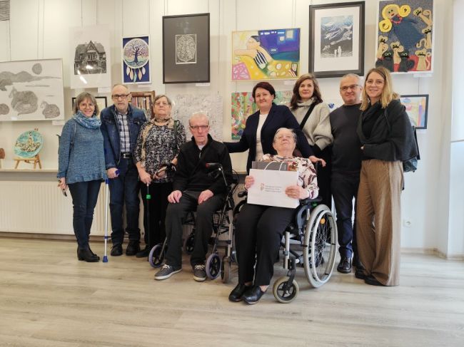 Powiększ zdjęcie: grupa osób podczas wystawy na tle prac wiszących naścianie