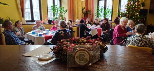 Powiększ zdjęcie: wnętrze kawiarni dps, na pierwszym planie stroik świąteczny, w tle Mieszkańcy przy stolikach