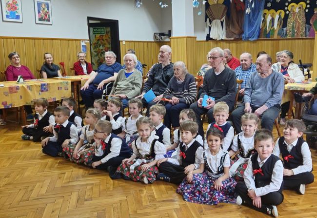 Powiększ zdjęcie: grupa przedszkolaków i Mieszkańcy "Pogodnej Jesieni" w jadalni dps